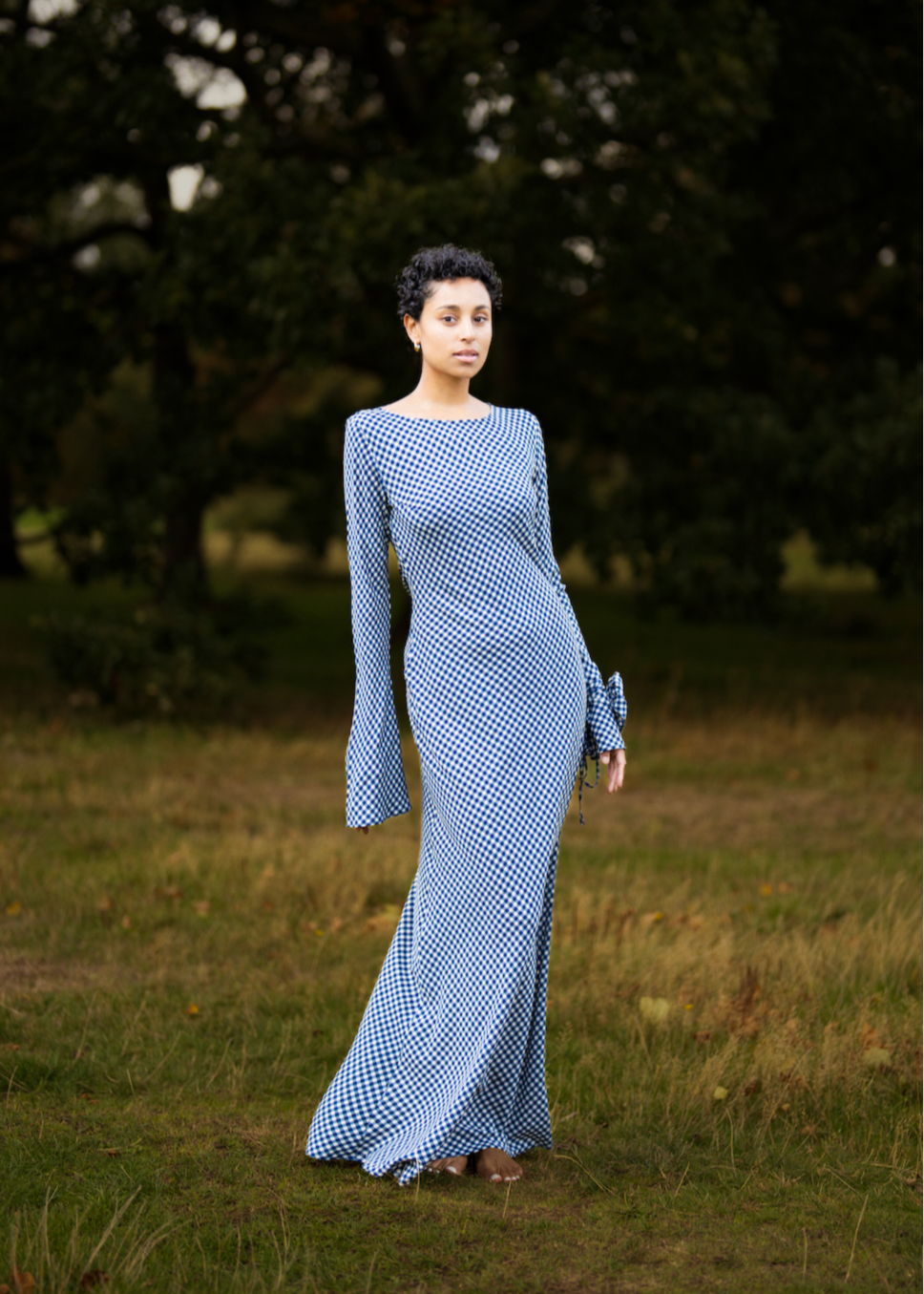 Woman in a long blue dress standing in a grassy field with trees in the background